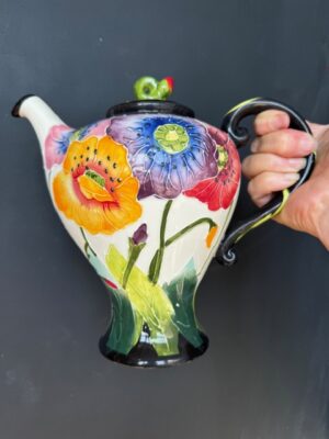 a hand holding a Blue Sky Clayworks Teapot covered in multicoloured poppies