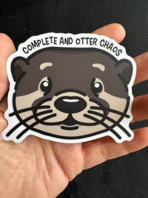 Hand holding a sticker with an otter's face, and text "Complete and otter chaos"