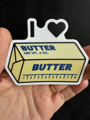 Hand holding a sticker with a wrapped butter stick, and text "I (heart) butter"