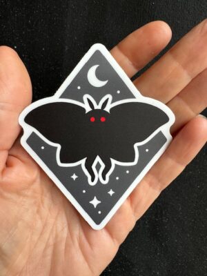 Hand holding a sticker with black mothman on a starry night sky