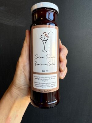 A bottle of Round Box Foods Cocoa Sauce being held by a hand