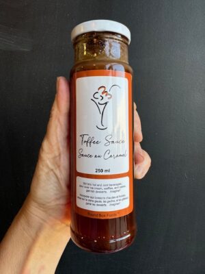 A bottle of Round Box Foods Toffee Sauce being held by a hand