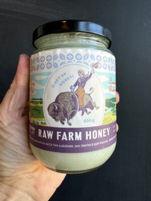 A jar of The Saskatoon Farm Honey, 500 ml being held by a hand