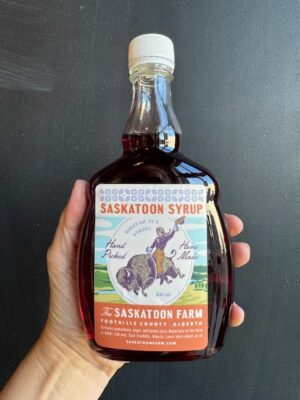 A jar of The Saskatoon Farm Syrup being held by a hand