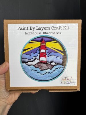 Shadow Box painting kit called Lighthouse featuring a lighthouse on a rock with its light shining over the water