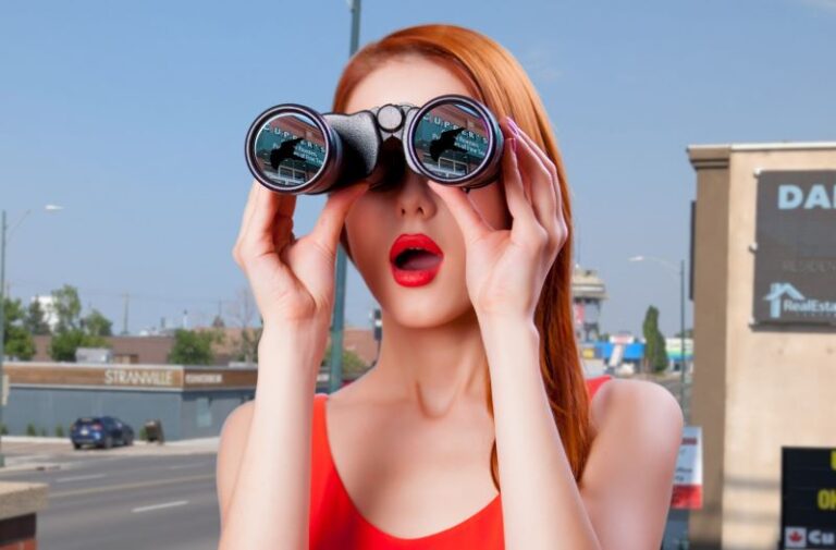 A woman in red with binoculars that show a bird against the Cupper's sign