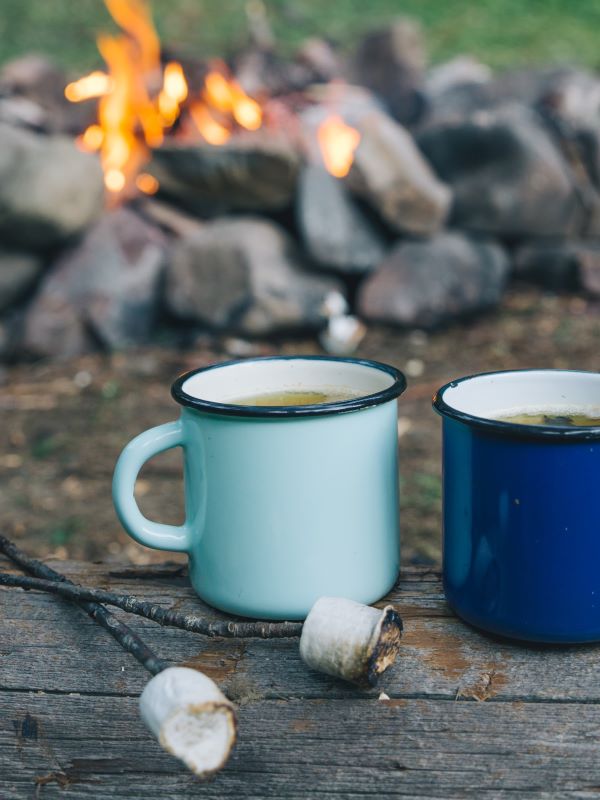 Hot drinks in enamel mugs and roasted marshmallows on a stick in front of a campfire