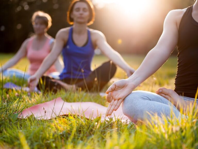 Three people sitting, meditating and doing yoga in a grassy park