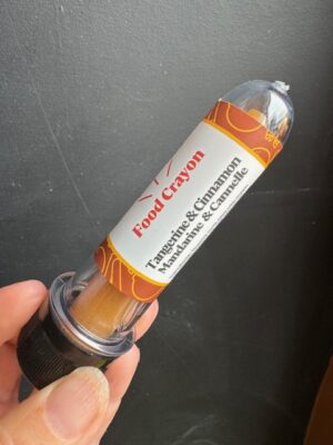 Tangerine & Cinnamon Food crayon in front of a black background