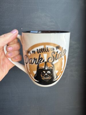 cream mug with black interior, featuring face of Darth Vader over gold logo, and black text "I like my coffee on the Dark Side."