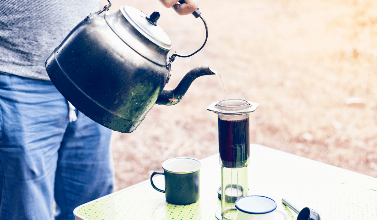 outside camp kettle pouring hot water into Aeropress Coffee Maker on a picnic table