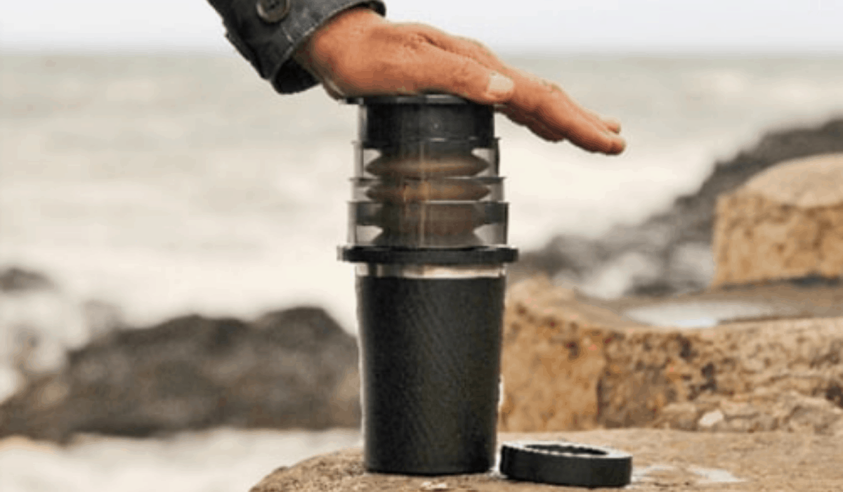 Cafflano Kompact Coffee Maker being pressed on a large rock on a blurred beach background