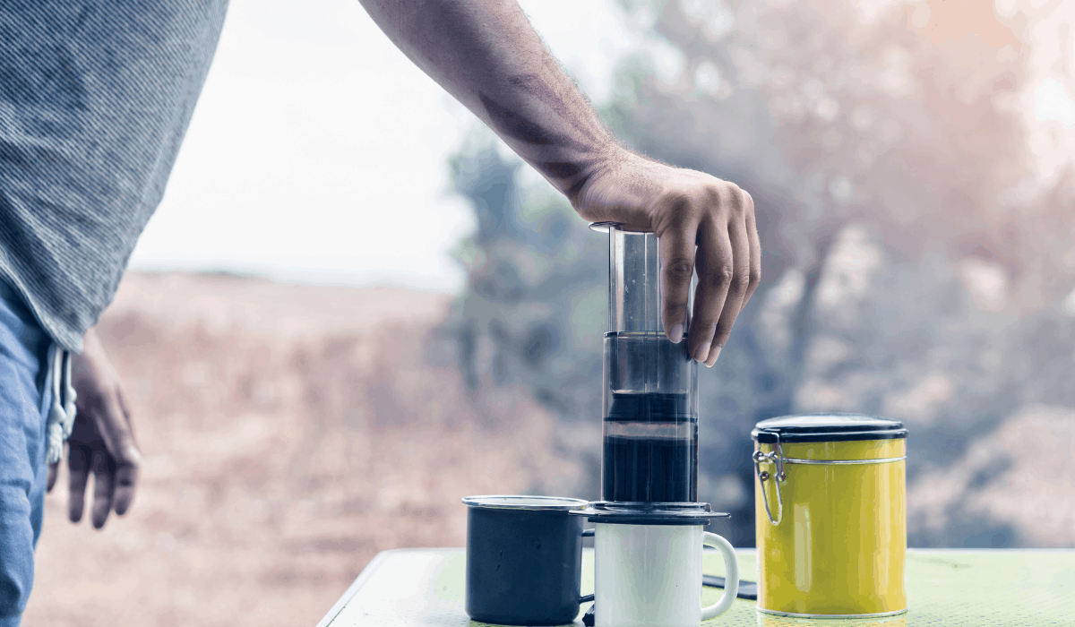 Man outside pressing down on Aeropress Coffee Maker over a mug on a picnic table