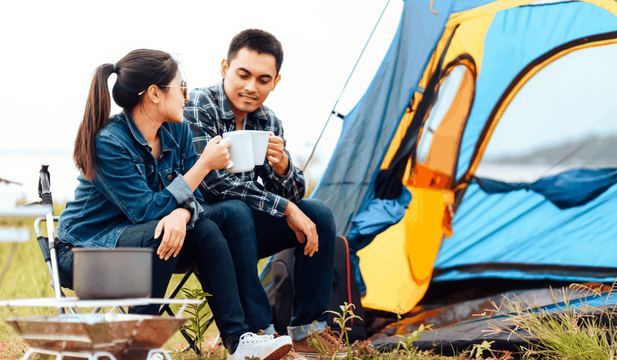 camping Man and woman sitting at a campsite, blue tent, stovepot and clinking coffee mugs