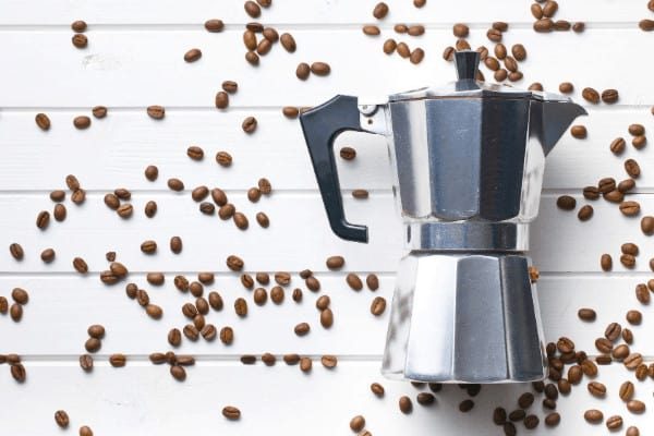 coffee makers Bialetti lying on a white plank table with coffee beans