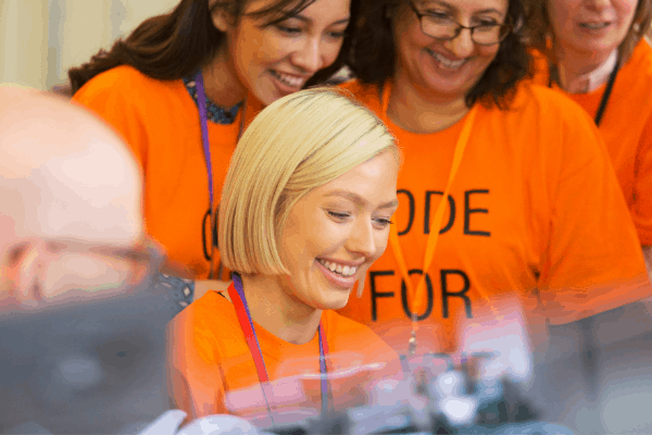 Three people looking over the shoulder of a seated woman, all in orange t-shirts and lanyards