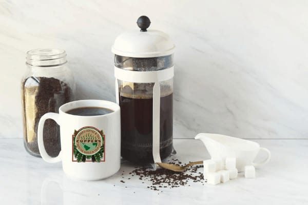 how to make coffee in a french press White French press full of coffee, with a jar of ground coffee, a cupper's mug with coffee, and sugar and cream beside