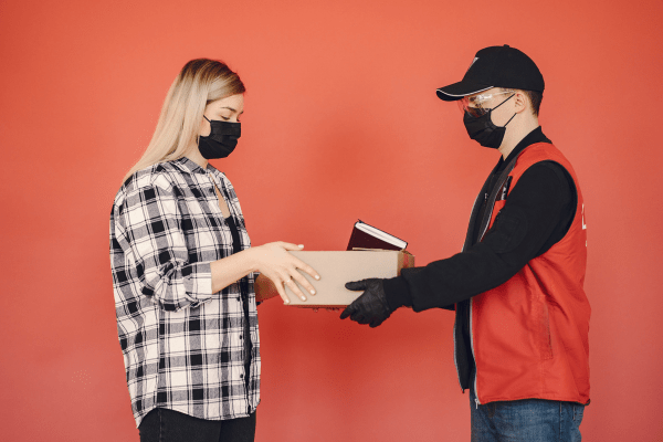 Masked delivery man handing a box to a masked woman